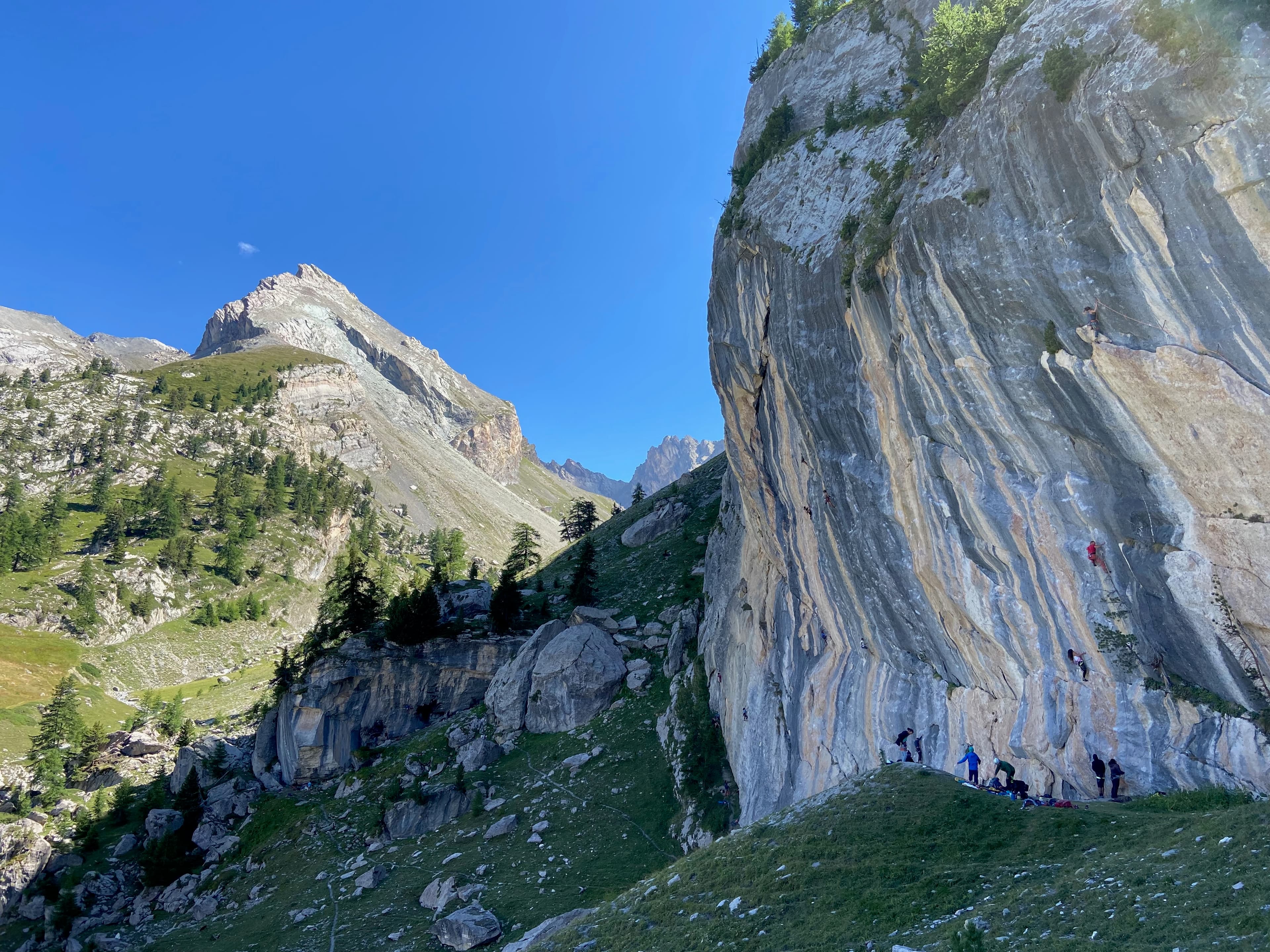 Large alpine climbing wall with climbers below a clear blue sky.