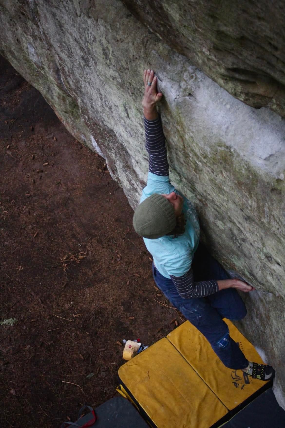 Tom bouldering on an outdoor gritstone roof above stacked crash pads.
