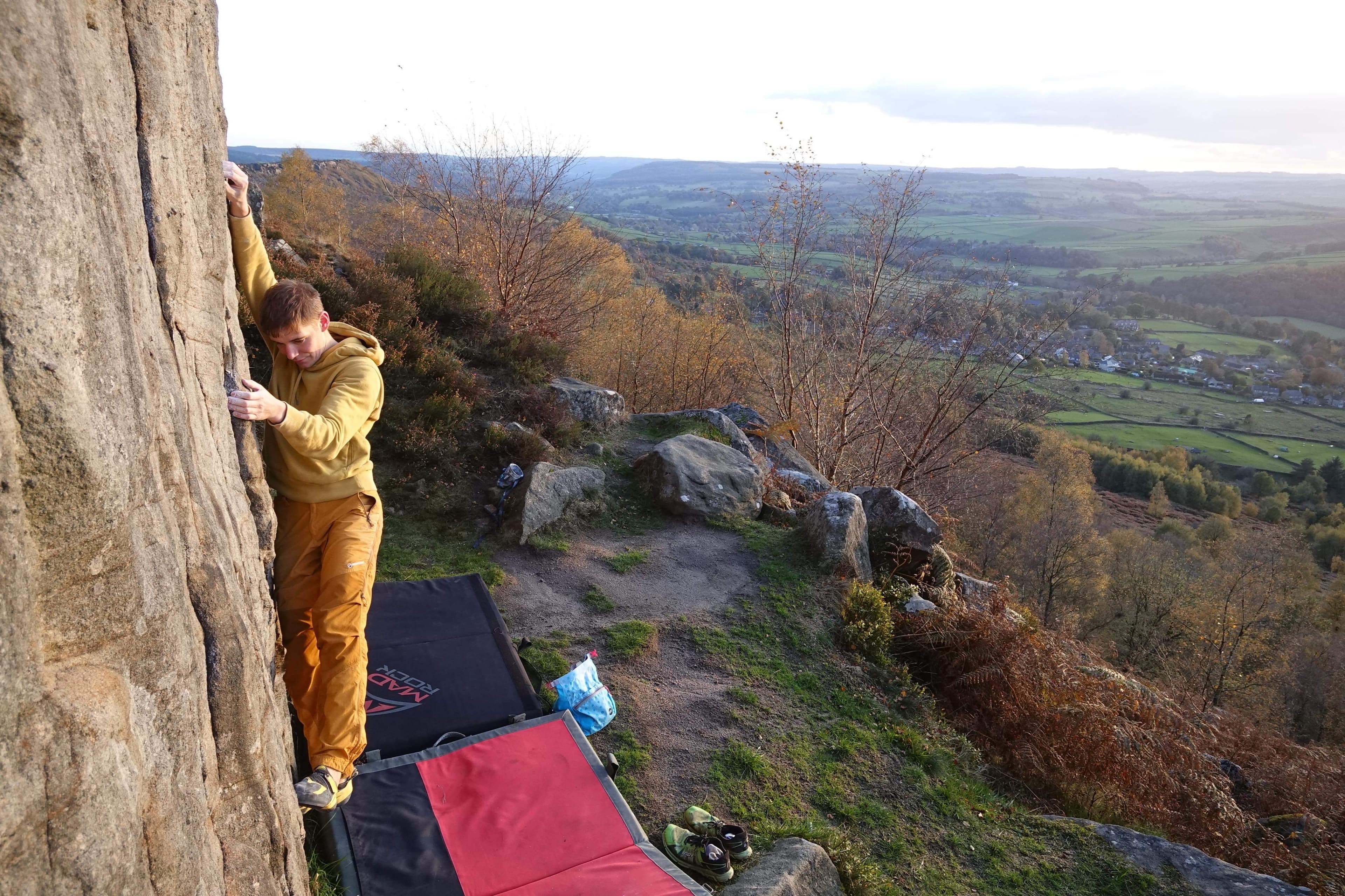 Tom bouldering outdoors on gritstone with the Peak District valley behind.
